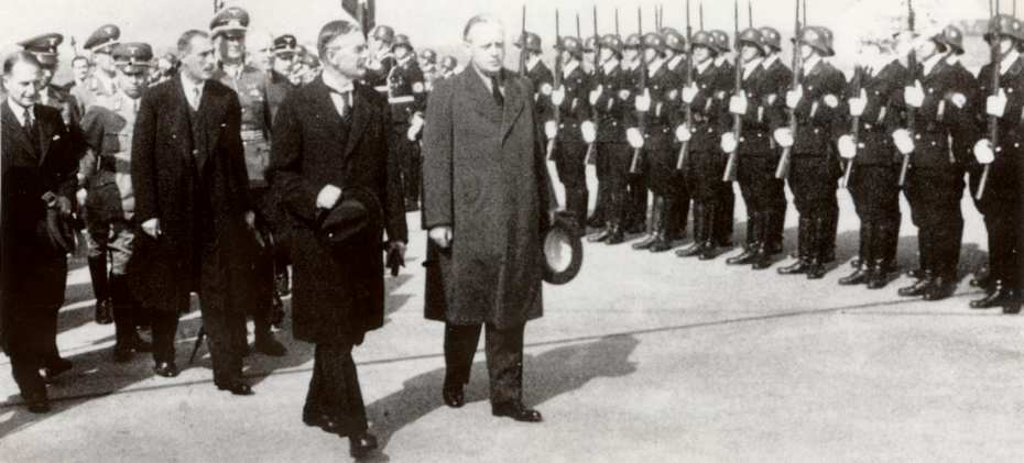 Premierminister Neville Chamberlaine schreitet mit Außenminister von Ribbentrop und Frhr. von Weizsäcker die Ehrenkompanie auf dem Flughafen Köln Butzweilerhof ab.